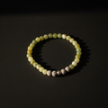 A beaded stretch bracelet made of pale yellow-green and white marbled beads, accented by three textured metallic spacer beads, photographed on a dark background with dramatic side lighting.