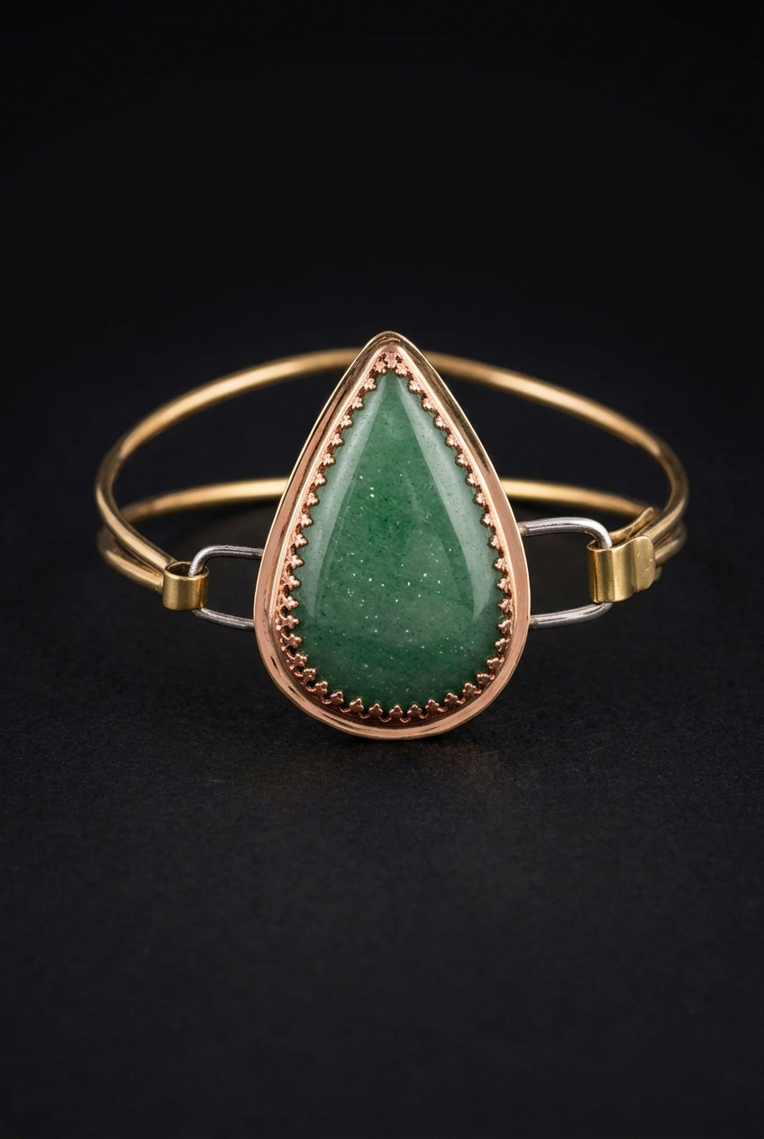 Handcrafted mixed-metal bangle bracelet featuring a teardrop green aventurine cabochon set in a scalloped copper crown bezel with double brass wire bands and clasp loops, on a dark moody background.