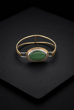 Direct top-down view of a handcrafted mixed-metal oval bangle bracelet showcasing a smooth green aventurine gemstone in a multi-tonal bezel and double brass wire frame on a dark slate surface.