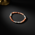 A beaded stretch bracelet featuring peach, orange, and pale pink round beads, accented with white translucent beads and textured silver spacer beads, displayed on a dark background.