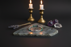 A beaded bracelet with green, purple, and white beads rests on a gray stone slab, styled with lavender sprigs, raw crystal clusters, and two lit gold candlesticks against a dark background.