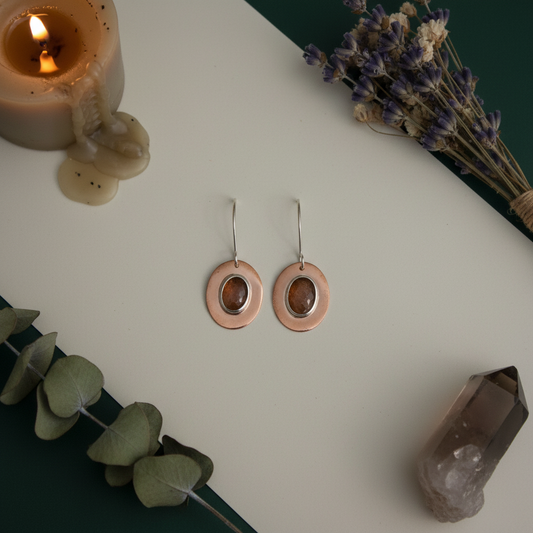 Solar Ember Earrings by Jewellery by JN, featuring oval peach sunstone cabochons bezel-set in fine silver on polished copper discs with sterling silver ear wires.