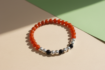 Beaded bracelet with orange, silver, and black beads on a beige and green background