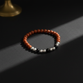 A beaded stretch bracelet with orange-red round beads, separated by small silver and black beads, displayed on a dark surface with dramatic side lighting.