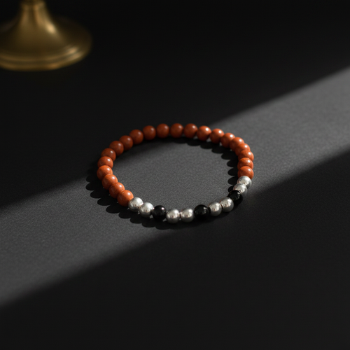 A beaded stretch bracelet with orange-red round beads, separated by small silver and black beads, displayed on a dark surface with dramatic side lighting.