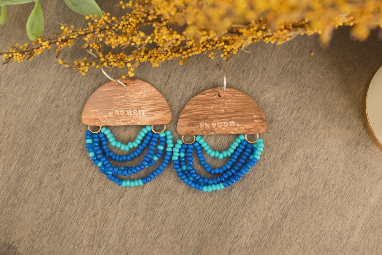 Edit this close-up to highlight the texture, metalwork, and gemstone details of the earrings. Use soft, directional lighting and a subtle, blurred background in brand colours. Enhance the sense of warmth, artisanal quality, and soulful craftsmanship, but do not change the physical appearance, shape, or colour of the earrings.
