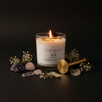 A lit glass jar candle labeled 'Full Moon Intuitive Candles' sits on a dark surface with crystals, dried flowers, and a gold-colored wick remover nearby against a black background.