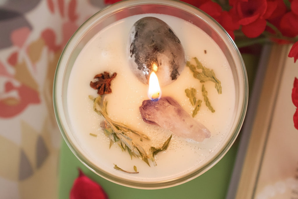 Candle in a tin with floating botanicals and a lit wick, surrounded by flowers.