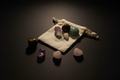 A set of polished crystal stones in various colors, including pink, purple, green, and brown, arranged around a small cream-colored drawstring pouch on a dark, reflective surface.