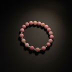 A beaded stretch bracelet made of pink and white polished round beads separated by small silver spacer beads, displayed on a dark background.