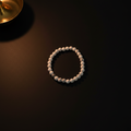 A beaded bracelet made of small round off-white beads, arranged in a circle on a dark surface with warm ambient lighting.