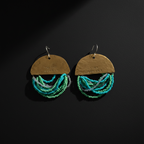 A pair of handmade dangle earrings on a dark background. Each earring features a hammered brass semi-circle top with the words 'YOU ARE LOVED BY' and '1 ST FOREVER' engraved, with multiple strands of turquoise, teal, and green seed beads hanging below.