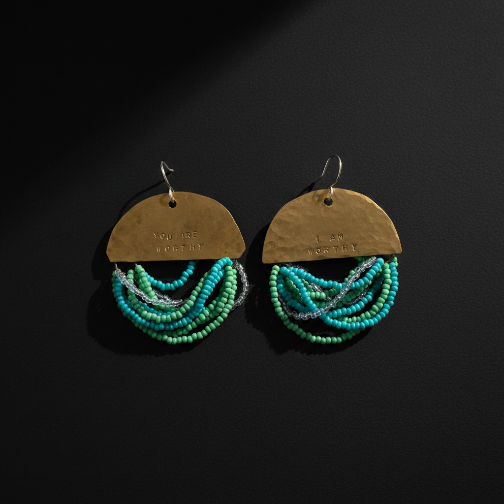 A pair of handmade dangle earrings on a dark background. Each earring features a hammered brass semi-circle top with the words 'YOU ARE LOVED BY' and '1 ST FOREVER' engraved, with multiple strands of turquoise, teal, and green seed beads hanging below.