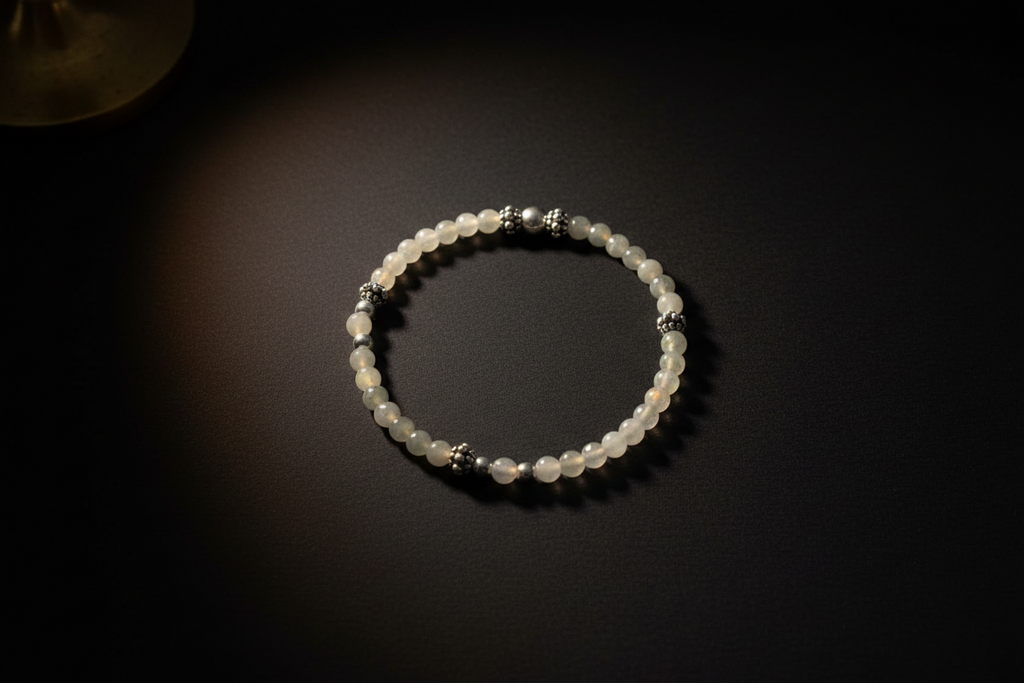 A beaded bracelet made of translucent white beads with small silver spacer beads, displayed on a dark background under warm spotlighting.