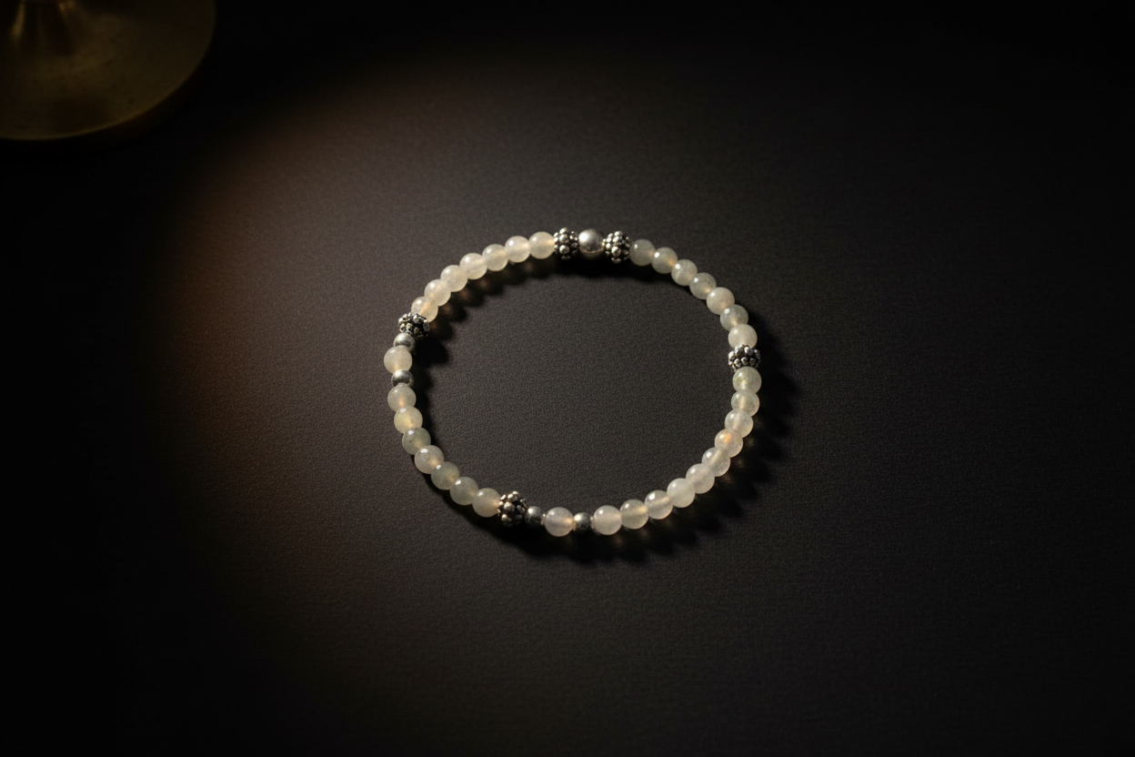 A beaded bracelet made of translucent white beads with small silver spacer beads, displayed on a dark background under warm spotlighting.
