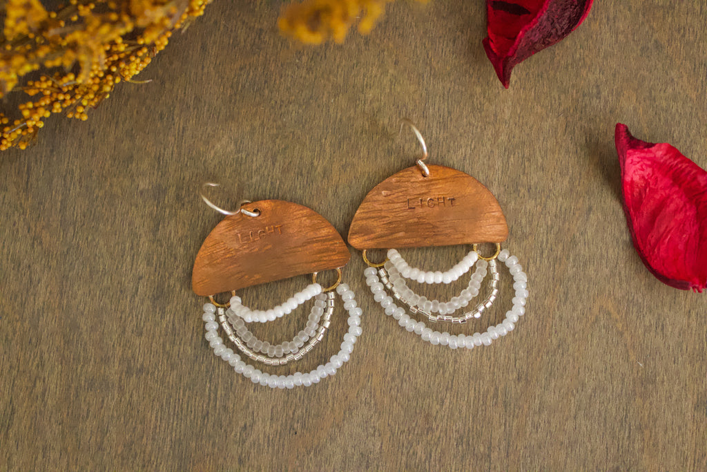 Close-up of Mini Wordkeeper Earrings Light by Jewellery by JN, highlighting textured copper, white and silver beadwork, and hand-stamped word LIGHT.