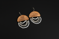 A pair of handmade dangle earrings featuring engraved wooden semicircles with the word 'Light' on them, hanging from gold-toned fishhook wires. Below the wood pieces are multiple layers of white and silver beaded fringe, set against a solid black background.