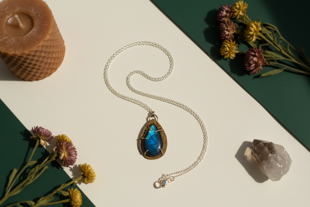 Necklace with a blue pendant on a white surface with flowers and a crystal.