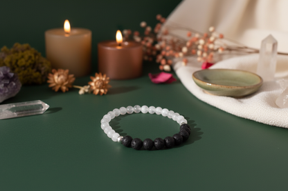 Bracelet with black and white beads on a green surface with candles and crystals in the background