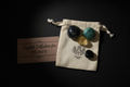 Four polished gemstone crystals displayed on a cream drawstring pouch next to a pink card that reads 'Crystal Collection for Money', set against a dark black background.