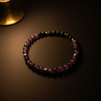A beaded stretch bracelet featuring purple amethyst, black obsidian, and silver-colored metallic beads, displayed on a dark brown textured surface under warm, moody lighting.