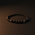A beaded bracelet made of dark, textured round beads arranged in a circle on a dark brown surface.