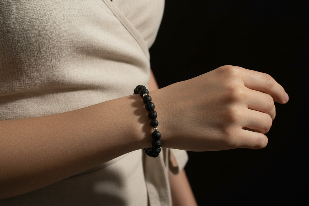 A close-up of a person's wrist wearing a dark beaded bracelet, with a light beige linen top and a solid black background.