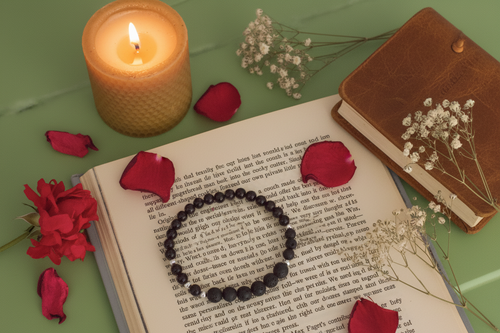 Open book with a bracelet, candle, and flowers on a green surface