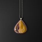 A teardrop-shaped pendant necklace featuring a polished yellow and reddish-brown agate stone set in a silver-toned bezel, suspended from a thin silver chain against a dark background.