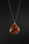 A teardrop-shaped pendant necklace featuring a polished red and orange agate stone with yellow inclusions, set in a rose gold bezel on a delicate silver chain, presented against a dark background.