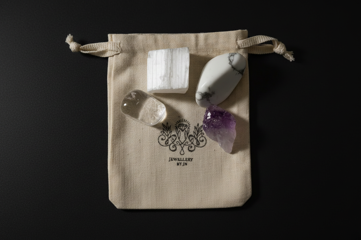 Four raw crystal stones arranged on a beige fabric drawstring pouch with a black printed logo that reads 'JEWELLERY BY J.R.