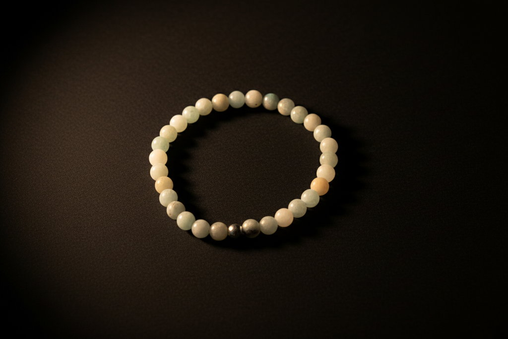 A beaded stretch bracelet made of matte off-white and pale green round beads, with a small metallic silver accent bead, displayed on a dark background.