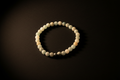 A beaded stretch bracelet made of matte off-white and pale green round beads, with a small metallic silver accent bead, displayed on a dark background.