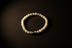 A beaded stretch bracelet made of matte off-white and pale green round beads, with a small metallic silver accent bead, displayed on a dark background.