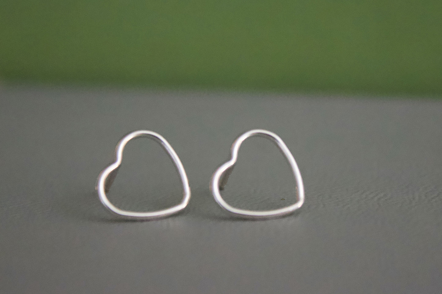 Heart-shaped silver earrings on a gray surface with a green background