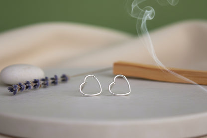 Heart-shaped silver earrings on a gray surface with a green background