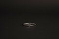 A minimalist silver band ring with a small, polished heart-shaped charm in the center, resting on a dark, textured surface.