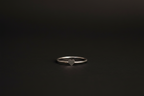 A minimalist silver band ring with a small, polished heart-shaped charm in the center, resting on a dark, textured surface.