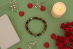 Bracelet on a green surface with red flowers and a lit candle