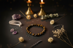 A beaded bracelet made of brown and gold tiger's eye beads is arranged on a dark surface with crystals, dried flowers, lavender, and two lit brass candlesticks in the background.