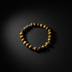 A beaded stretch bracelet featuring round brown and yellow tiger's eye beads accented with small metallic silver beads, displayed on a dark black background.