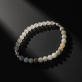 A beaded stretch bracelet made of translucent white and pale green gemstone-like beads with a few metallic silver spacer beads, photographed on a dark surface with dramatic shadows.