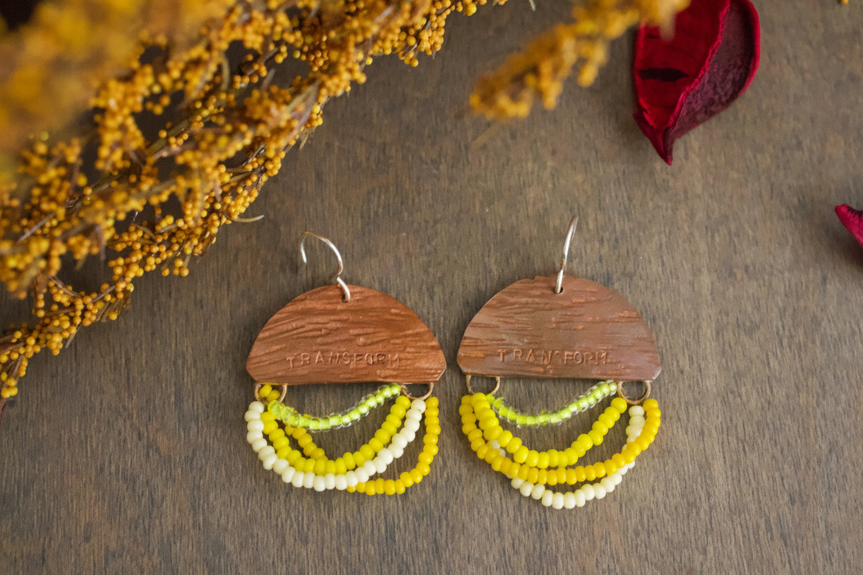 Wooden earrings with colorful beaded strands on a wooden surface with dried flowers.