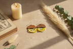 Pair of earrings on a textured surface with a candle and dried plants in the background