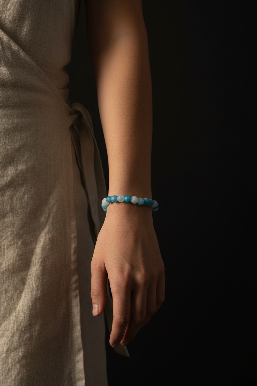 A person wearing a beaded bracelet with light blue and white round beads, shown against a dark background.