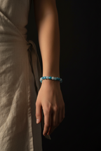 A person wearing a beaded bracelet with light blue and white round beads, shown against a dark background.