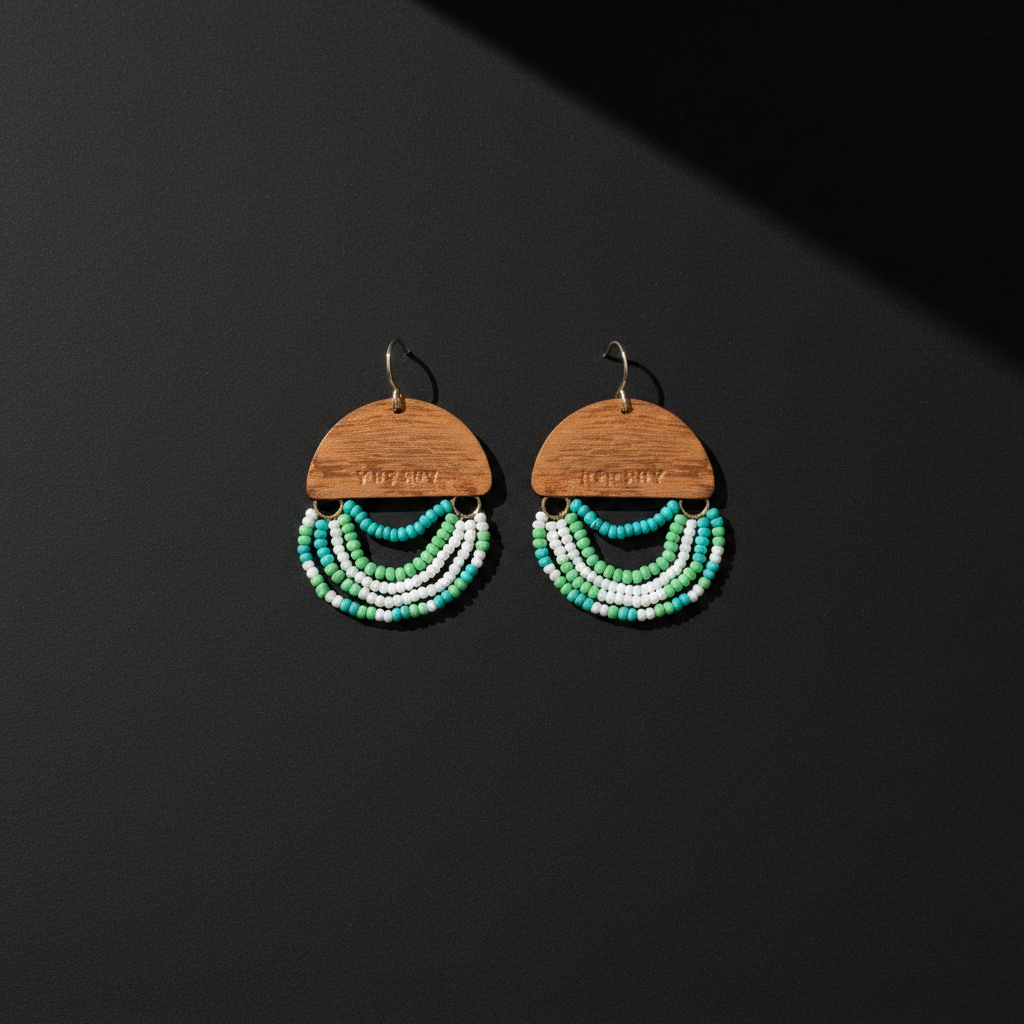 A pair of handmade dangle earrings featuring a semi-circular wooden top piece with the brand name 'THE BEADY' engraved, adorned with three curved rows of small beads in white, turquoise, and green, hanging against a dark gray background.