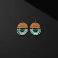 A pair of handmade dangle earrings featuring a semi-circular wooden top piece with the brand name 'THE BEADY' engraved, adorned with three curved rows of small beads in white, turquoise, and green, hanging against a dark gray background.