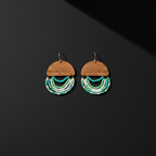 A pair of handmade dangle earrings featuring a semi-circular wooden top piece with the brand name 'THE BEADY' engraved, adorned with three curved rows of small beads in white, turquoise, and green, hanging against a dark gray background.