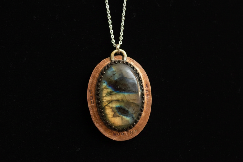 A handmade oval pendant necklace featuring a polished labradorite stone with a blue and gold sheen, set in a copper-toned bezel with a silver-toned chain against a solid black background.